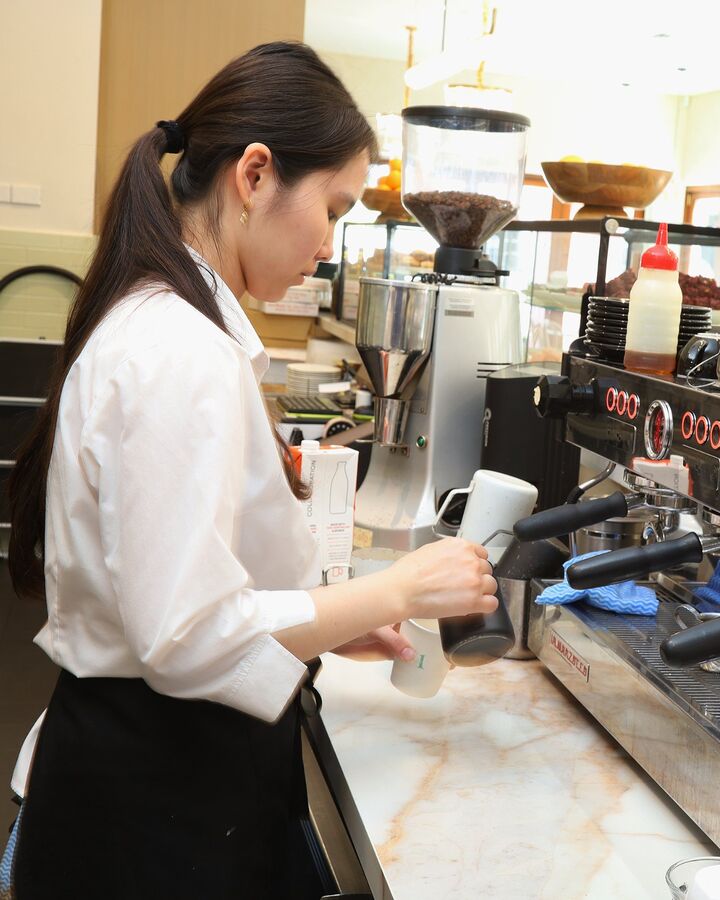 A barista pouring milk at the coffee machine