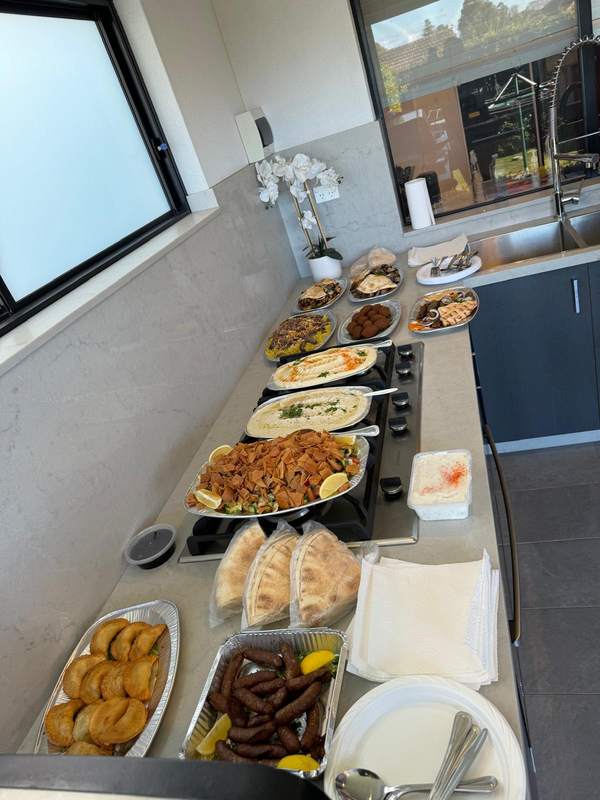 A party spread on a kitchen bench: sambusik, sujuk, fattoush, dips, falafel and wraps
